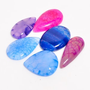 May include: Six polished gemstones in shades of blue, pink, and purple, with unique veining patterns. The stones are in various shapes. The gemstones are displayed on a white surface.