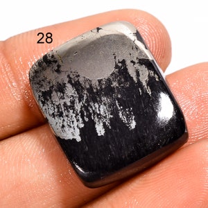May include: A black and silver gemstone cabochon with a rough, textured surface. The stone has a unique pattern of silver veins running through it. The stone is labeled "28".