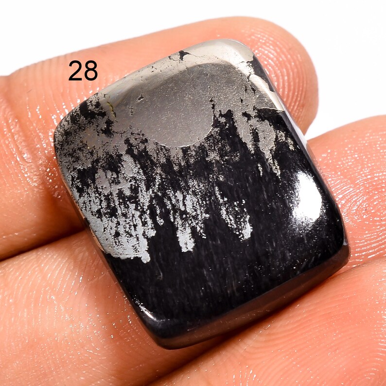 May include: A black and silver gemstone cabochon with a rough, textured surface. The stone has a unique pattern of silver veins running through it. The stone is labelled "28".
