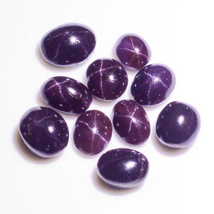 Puede incluir: Una colección de diez piedras preciosas ovaladas de color púrpura oscuro con un patrón en forma de estrella en el centro.