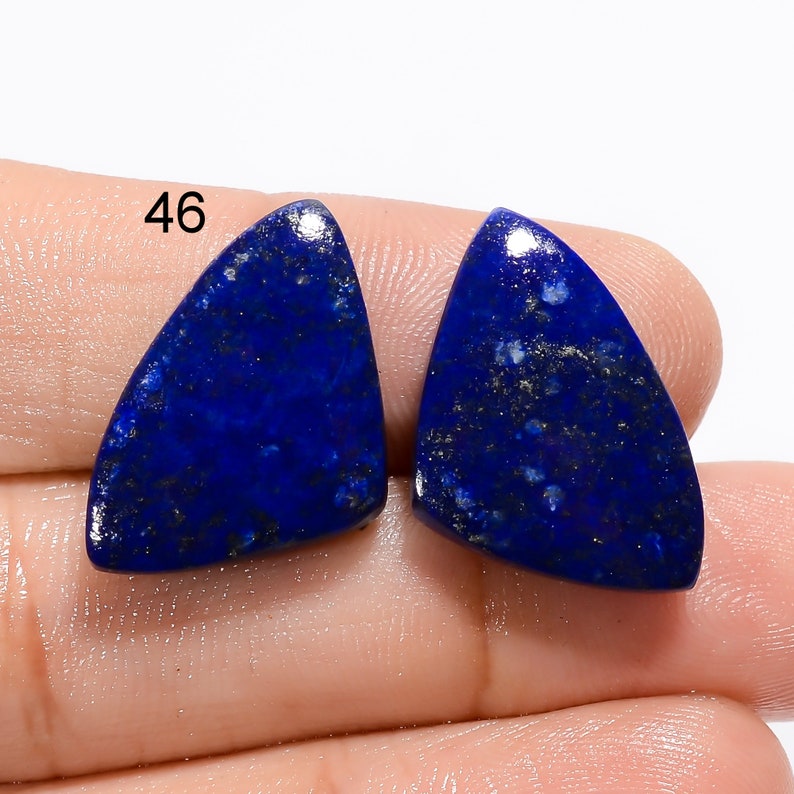 Op de afbeelding: Twee driehoekige lapis lazuli cabochons met een donkerblauwe kleur en gouden vlekken. De stenen zijn ongeveer 2,5 cm lang.