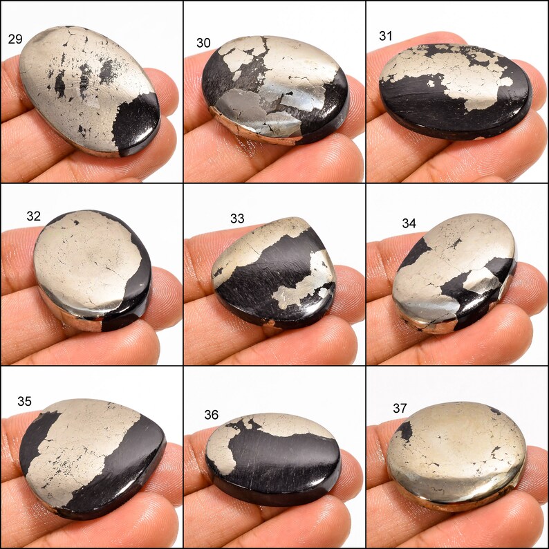 May include: A collection of nine oval and teardrop shaped cabochons of pyrite, a metallic mineral with a gold and black colour. The cabochons are displayed on a hand.