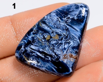 May include: A polished, triangular-shaped pietersite gemstone featuring a deep blue colour with swirling, chatoyant patterns of white and light blue fibres, along with small patches of brown mineral inclusions and the number 1.