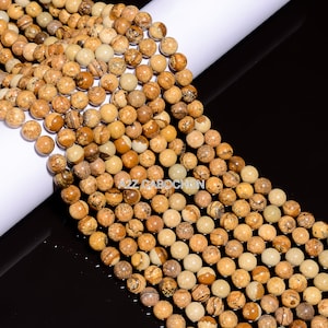 May include: A strand of brown and beige gemstone beads. The beads are round and have a speckled pattern. The beads are strung on a clear thread. The strand is approximately 10 inches long.