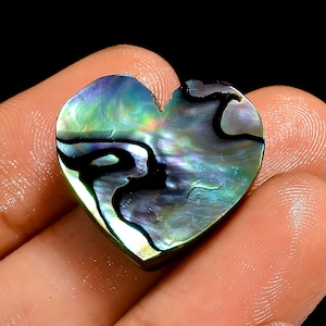 May include: A heart-shaped abalone shell with iridescent colors of green, blue, and black. The polished surface reflects light, showcasing the natural patterns and textures of the shell. The heart shape is smooth and well-defined, perfect for jewelry or crafts.