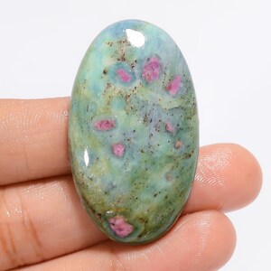 Può includere: Pietra preziosa ovale a cabochon con un motivo di colore verde, blu e rosa. La pietra ha una superficie liscia e lucida.