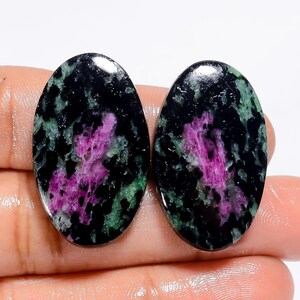 Puede incluir: Dos piedras preciosas ovaladas con un patrón negro, verde y rosa. Las piedras son opacas y tienen un aspecto moteado.