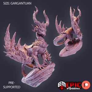 May include: Two 3D printed dragon miniatures in a light pink color. The dragons are in a standing pose with wings spread. The text "SIZE: GARGANTUAN" and "PRE-SUPPORTED" are visible in the image.
