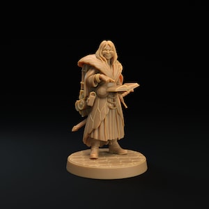 Op de afbeelding: Een bruin gekleurde miniatuurfiguur van een fantasiekarakter, mogelijk een tovenaar of geleerde, die een boek vasthoudt. De figuur draagt een lange jurk, een rugzak en een zwaard. De figuur staat op een cirkelvormige basis met een zeshoekig patroon.
