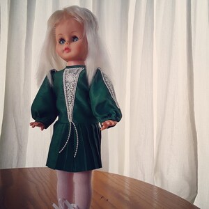 K&ouml;nnte beinhalten: Eine Vintage-Puppe mit wei&szlig;en Haaren und blauen Augen, die ein gr&uuml;nes Kleid mit wei&szlig;en Spitzenbesatz und wei&szlig;en Schuhen tr&auml;gt.