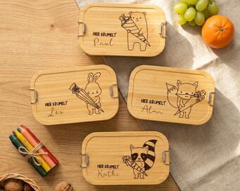 May include: Four rectangular bamboo lunch boxes with rounded corners and metal side latches. Each lid features a laser-engraved animal illustration holding a cone, the text "HIER KRUMELT" and a name: Paul with a bear, Leo with a rabbit, Alma with a fox, and Kathi with a raccoon.