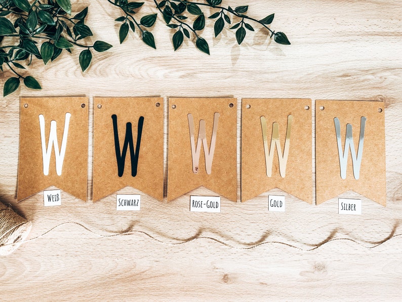 May include: Five brown paper pennant flags with the letter "W" in different colors. The flags are labeled "WEISS", "SCHWARZ", "ROSE-GOLD", "GOLD", and "SILBER".