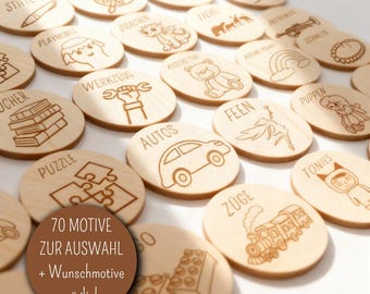 May include: A collection of wooden discs with engraved illustrations and text. The discs feature various images, including a car, puzzle pieces, a train, and a teddy bear. The text on the discs is in German. A circular graphic states "70 MOTIVE ZUR AUSWAHL + Wunschmotive möglich."