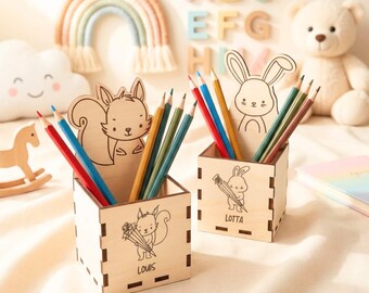 May include: Two square light-colored wooden pencil holders featuring laser-engraved animal designs. One holder displays a squirrel with the name "LOUIS" and a squirrel cutout, while the other shows a rabbit with the name "LOTTA" and a rabbit cutout.