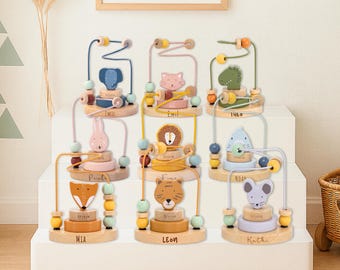 May include: A collection of wooden bead mazes featuring animal designs, including an elephant, cat, alligator, rabbit, lion, fox, tiger, and mouse. Each maze has a unique color scheme and a child's name. The mazes are displayed on a white stepped surface.