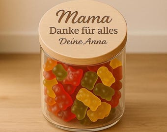 May include: A clear glass jar filled with colorful gummy bears. The jar has a wooden lid with the words "Mama Danke für alles Deine Anna" engraved on it. The gummy bears are red, yellow, and green.