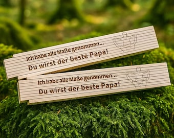 May include: Two wooden signs with the text "Ich habe alle Maße genommen... Du wirst der beste Papa!"  The signs are on a bed of green moss.