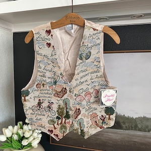 Peut inclure: Gilet beige en tapisserie sur le thème italien, avec des illustrations d'arbres, de maisons et de personnes. Le gilet a une fermeture boutonnée et est suspendu à un cintre en bois. Le gilet contient du texte en italien.