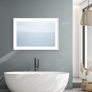 May include: A modern bathroom with a white oval bathtub, a framed seascape print, and a black faucet. The walls are painted a muted teal, and the floor is concrete. A woven pendant light hangs from the ceiling, and decorative vases add a natural touch.