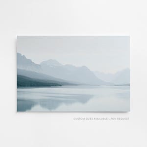 Puede incluir: Una impresi&oacute;n de paisaje que presenta una serena escena lacustre con monta&ntilde;as al fondo. La obra de arte est&aacute; dominada por tonos de azul y gris, creando una est&eacute;tica calmante y atmosf&eacute;rica. El texto "CUSTOM SIZES AVAILABLE UPON REQUEST" es visible en la parte inferior.