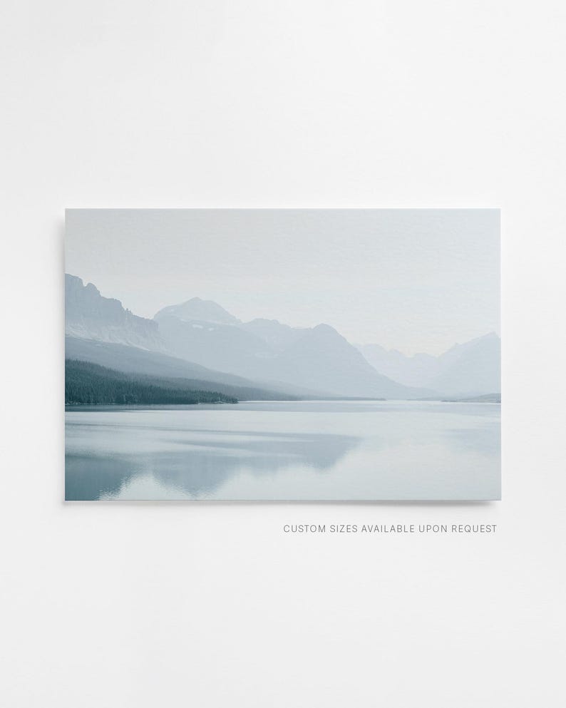 Puede incluir: Una impresi&oacute;n de paisaje que presenta una serena escena lacustre con monta&ntilde;as al fondo. La obra de arte est&aacute; dominada por tonos de azul y gris, creando una est&eacute;tica calmante y atmosf&eacute;rica. El texto "CUSTOM SIZES AVAILABLE UPON REQUEST" es visible en la parte inferior.