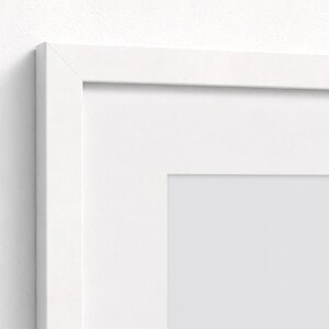 Puede incluir: Primer plano de un marco de fotos blanco con un paspart&uacute; blanco. El marco tiene un dise&ntilde;o sencillo y limpio con forma rectangular. El marco est&aacute; montado en una pared blanca.