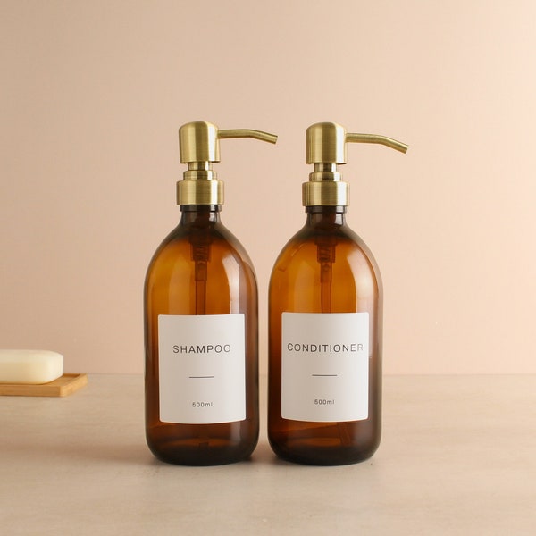 May include: Two amber glass bottles with gold pumps and white labels. The labels read "Shampoo 500ml" and "Conditioner 500ml".