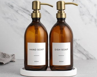 May include: Two amber glass soap dispensers with gold pumps, labeled "HAND SOAP" and "DISH SOAP" with a white label and black text. Each dispenser holds 500 ml of liquid soap and sits on a white oval tray.