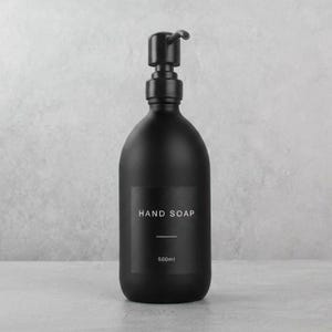 May include: A matte black hand soap dispenser with a pump. The label reads "HAND SOAP" and "500ml". The dispenser has a minimalist design and is likely made of ceramic or glass.