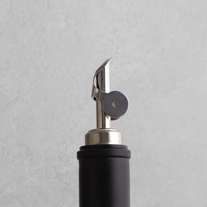 May include: A silver bottle pourer with a black bottle. The pourer has a spout and a ring around the top.