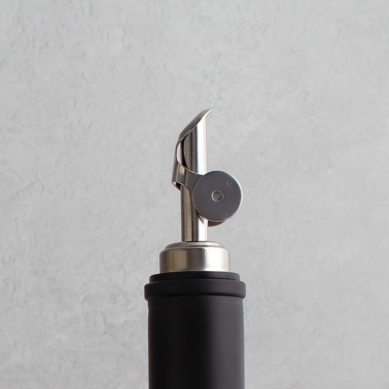 May include: A silver bottle pourer with a black bottle. The pourer has a spout and a ring around the top.