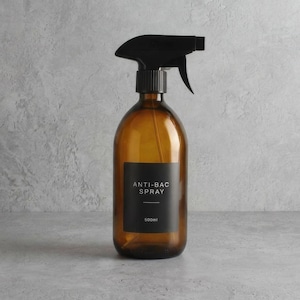 Pode incluir: Frasco de spray de vidro âmbar com bico preto. O frasco tem um rótulo preto que diz "ANTI-BAC SPRAY" e "500ml". O frasco está sobre uma superfície cinza.