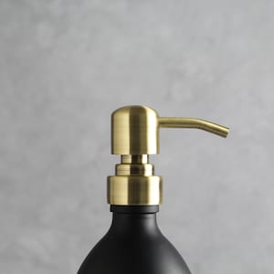 May include: A gold soap dispenser with a black bottle. The dispenser has a sleek, modern design and is perfect for any bathroom.