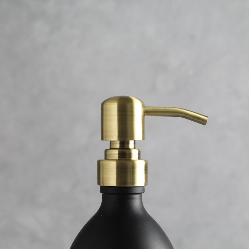 May include: A gold soap dispenser with a black bottle. The dispenser has a sleek, modern design and is perfect for any bathroom.