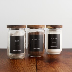 Puede incluir: Tres tarros de vidrio con tapas de madera y etiquetas negras. Las etiquetas dicen "TEA", "COFFEE" y "SUGAR". Cada etiqueta tambi&eacute;n incluye el texto "NAMIE HOME".
