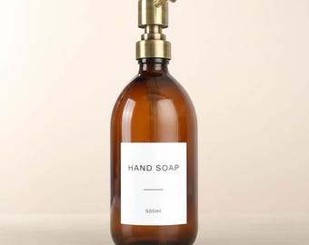 May include: Amber glass hand soap dispenser with a brass pump. The white label reads "HAND SOAP" and "500ml". The bottle has a rounded shape and is designed for liquid soap.