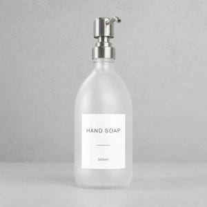 May include: Frosted glass hand soap dispenser with a silver metal pump. The white label reads "HAND SOAP" with a horizontal line and "500ml" below. The bottle is designed for liquid soap.