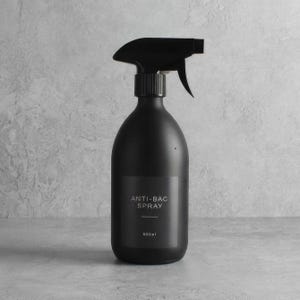 Könnte beinhalten: Eine mattschwarze Sprühflasche mit schwarzem Auslöser. Auf dem Etikett steht "ANTI-BAC SPRAY" und "500ml". Die Flasche hat eine abgerundete Form und ist zum Ausgeben von Flüssigkeit bestimmt. Der Hintergrund ist eine strukturierte graue Oberfläche.
