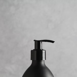 May include: A black pump bottle with a black cap and a silver pump. The bottle is on a gray background.