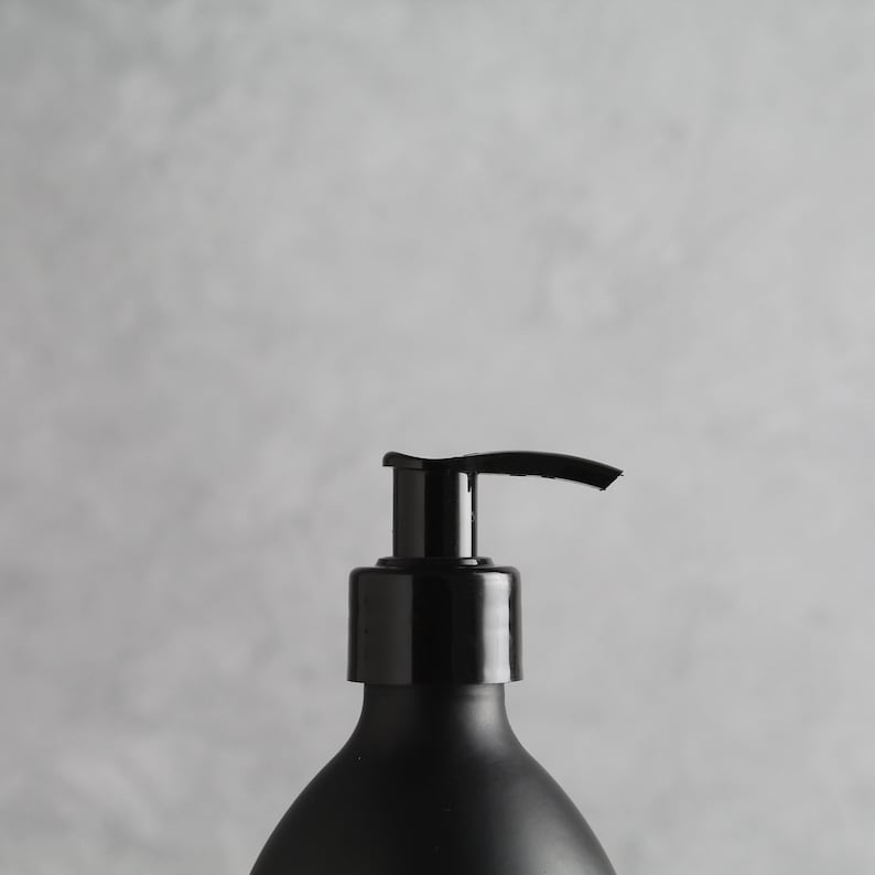 May include: A black pump bottle with a black cap and a silver pump. The bottle is on a gray background.