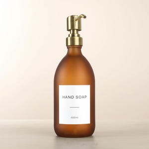 May include: A brown glass hand soap dispenser with a gold-coloured pump. The bottle has a white label with the words "HAND SOAP" and a 500ml capacity. The dispenser is designed for liquid soap.