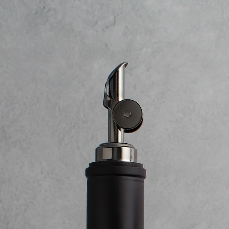 May include: A black and silver bottle pourer with a lever to control the flow of liquid.