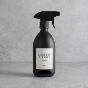 Könnte beinhalten: Eine mattschwarze Sprühflasche mit schwarzem Auslöser. Ein weißes Etikett auf der Vorderseite trägt die Aufschrift "BATHROOM CLEANER" und "500ml". Die Flasche hat eine abgerundete Form und ist für Reinigungsmittel konzipiert.