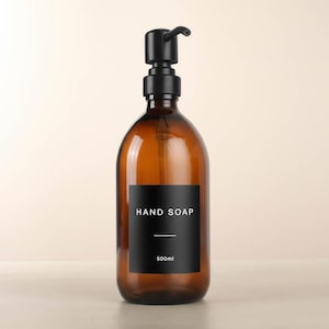 May include: Amber glass hand soap dispenser with a black pump and a black label. The label reads "HAND SOAP" and "500ml". The dispenser has a minimalist design.