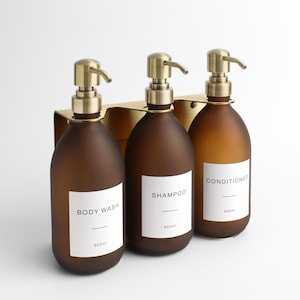 May include: Three brown glass bottles with brass pumps, labelled "Body Wash", "Shampoo", and "Conditioner". Each bottle holds 500ml and is mounted on a brass holder. The bottles have a frosted finish, ideal for a bathroom.