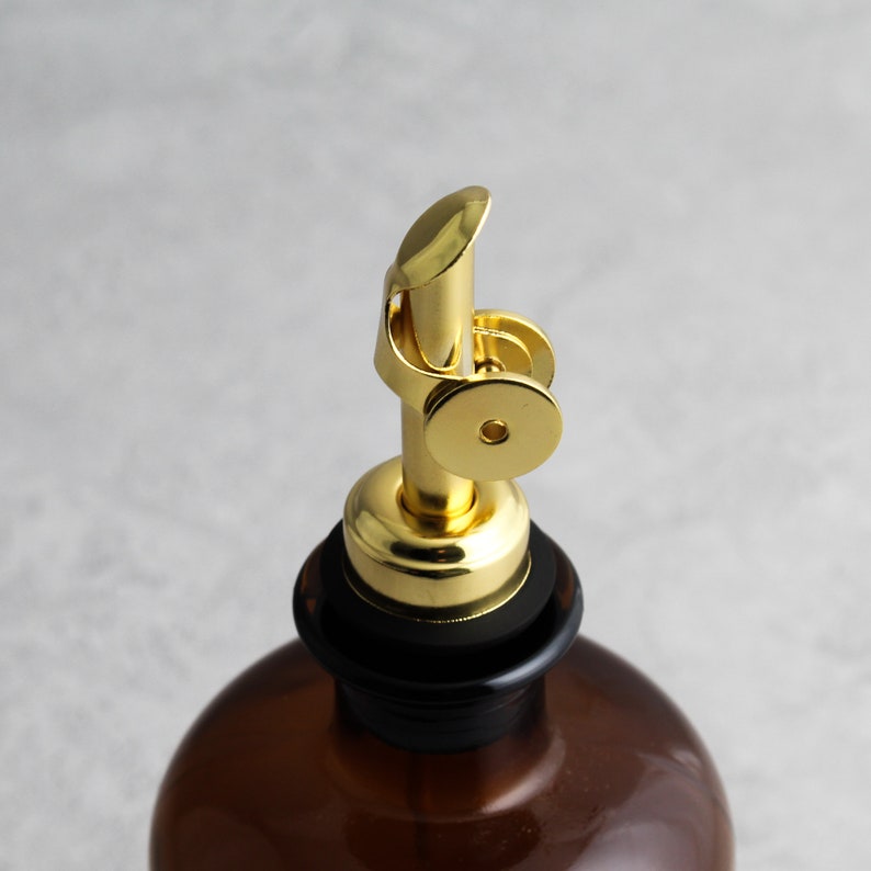 May include: A gold metal bottle stopper with a black rubber ring. The stopper has a spout with a lever that can be used to pour liquids.
