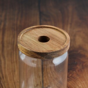 K&ouml;nnte beinhalten: Ein klares Glasgef&auml;&szlig; mit einem Holzdeckel. Der Deckel hat ein Loch in der Mitte.