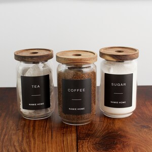 Puede incluir: Tres tarros de vidrio con tapas de madera y etiquetas negras. Las etiquetas dicen "TEA", "COFFEE" y "SUGAR". Cada etiqueta tambi&eacute;n incluye el texto "NAMIE HOME".