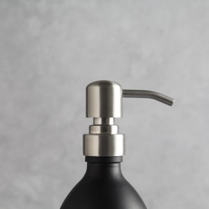 May include: A stainless steel soap dispenser pump with a black glass bottle. The pump has a long, curved spout.