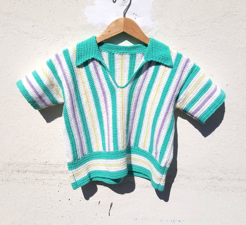 Puede incluir: Un top de crochet a rayas con cuello. El top es blanco con rayas verdes, amarillas y moradas.